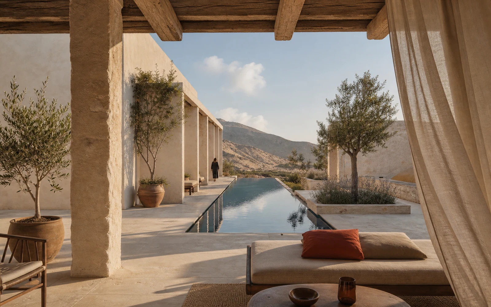 A limestone retreat courtyard with olive trees, linen curtains, and a narrow reflecting pool facing dry hills.